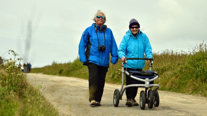 Two women walking along a path, one is using a walking aid at Trevose Head, Cornwall